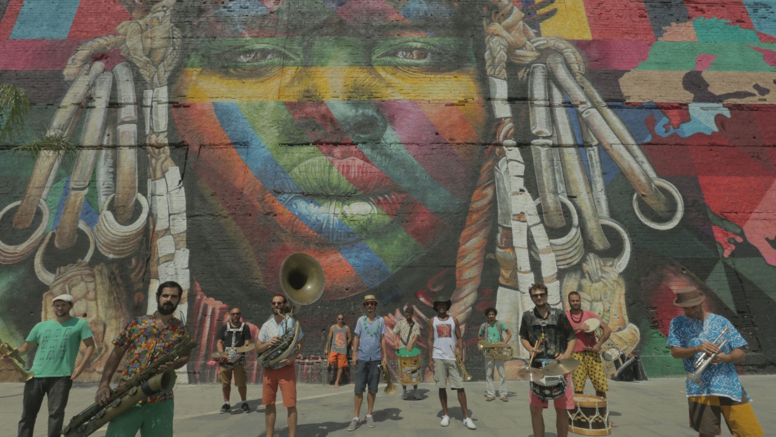 Pessoas com instrumentos musicais em frente a uma parede com um grande grafitti